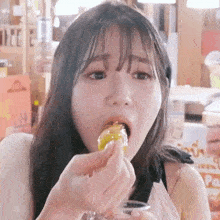 a young woman is eating a piece of food from a glass while looking at the camera .