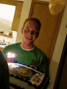 a man in a green shirt stands in front of a cake that says happy birthday