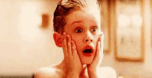 a young boy is holding his face with his hands and looking surprised .