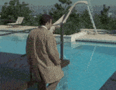 a man in a trench coat is standing next to a pool