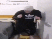a man wearing a black adidas shirt is sitting on a chair .