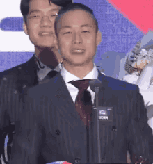 a man in a suit and tie is giving a speech in front of a microphone .