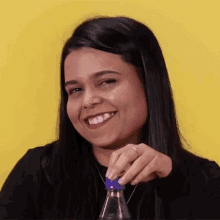 a woman is smiling while holding a bottle with a blue cap