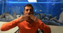 a man in an orange sweater is eating in front of a fish tank