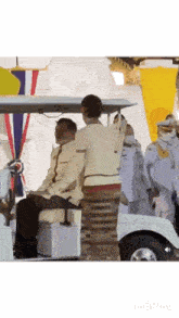 a man is sitting in a golf cart with a woman standing behind him .