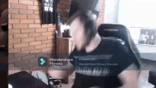 a man wearing headphones is sitting in a chair in front of a brick wall with wondershare filmora written on the screen