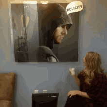 a woman sits in front of a painting of a man in a hood with the hashtag #olicity on it
