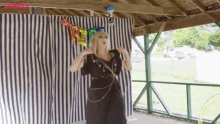 a woman in a black dress is standing in front of a striped curtain holding balloons that say happy birthday