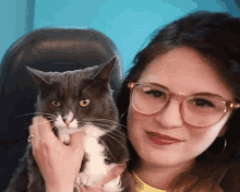 a woman wearing glasses is holding a cat