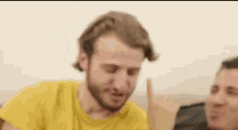 a man with a beard is sitting on a couch with another man and making a funny face .