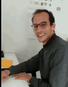 a man wearing glasses is smiling while sitting at a table