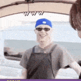 a man wearing sunglasses and a blue hat is standing next to another man in front of a car .