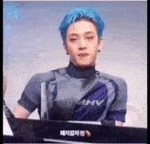 a man with blue hair is sitting at a desk with a fan in front of him .