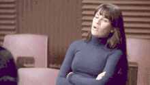 a woman in a blue turtleneck sweater is sitting with her arms crossed