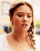 a woman wearing a braided ponytail and a necklace looks sad
