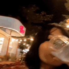 a woman is drinking water from a glass in front of a restaurant at night .