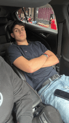 a man is sitting in the back seat of a car with his arms crossed and a graffiti wall in the background
