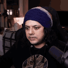a man with long hair wearing a purple hat and a black shirt