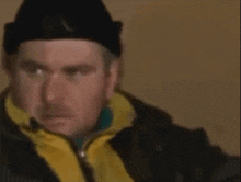 a man wearing a black hat and a yellow jacket is looking at the camera