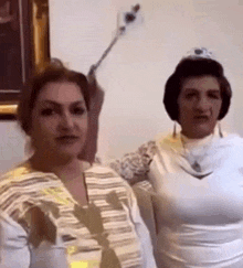 a couple of women are standing next to each other in a room . one of the women is wearing a tiara .