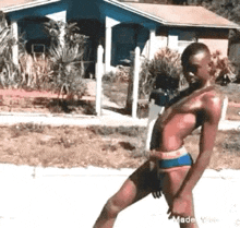 a man in a bathing suit is standing on a sidewalk in front of a house .