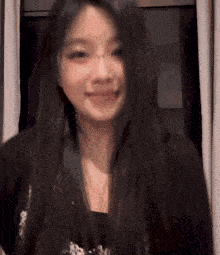 a woman with long black hair looks at the camera and smiles