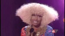 a woman in a wig is holding a microphone in front of a purple background .