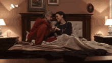a man and a woman are sitting on a bed with a hd logo on the corner