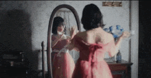 a woman in a red dress is standing in front of a mirror looking at herself .