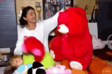 a woman is holding a large red teddy bear surrounded by stuffed animals