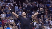 a man in a black shirt is raising his arms in the air in front of a crowd of people .