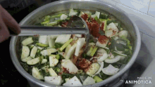a pot of vegetables is being stirred with tongs and the words made in animotica are on the bottom of the pot
