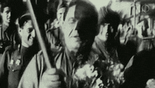 a man is holding a stick in front of a crowd of people in a black and white photo .