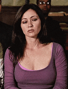a woman in a purple shirt is sitting in front of a group of people and looking at the camera .