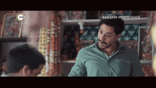 a man in a green shirt is talking to another man with the words kanjoos makhichoos on the bottom right