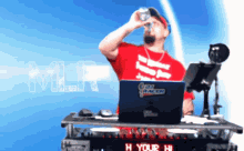 a man in a red shirt drinking from a can in front of a laptop that says dj racer