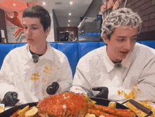 two men are sitting at a table with a large crab in front of them