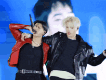 a man in a red jacket is singing into a microphone next to another man in a black shirt