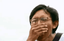 a man wearing glasses is covering his mouth with his hand while laughing .