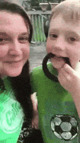 a woman in a green shirt with the word cake on it is holding a child in a green shirt with a soccer ball on it