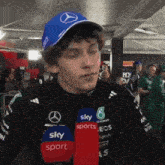 a man wearing a blue hat with a mercedes logo is talking into a microphone for sky sports