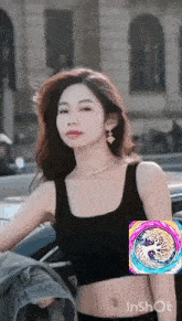 a woman in a black tank top is standing next to a car with a rainbow swirl on her belly