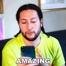 a man in a yellow shirt is holding a cell phone with the word amazing written on it