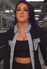 a woman with purple hair is wearing a black crop top and denim jacket