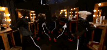 a group of people are dancing in front of a mirror in a dressing room .