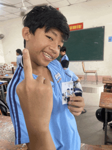 a boy in a blue shirt holds up his middle finger in front of a blackboard