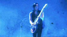 a man with long hair is playing a guitar in front of a blue backdrop