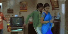a woman in a blue saree is standing next to a man in a green shirt and says " give me samantha "