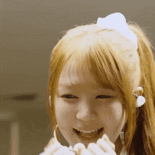 a girl with blonde hair and a white bow in her hair smiles