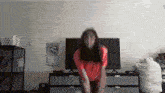a woman in a red shirt is dancing in front of a tv with a sticker on the wall that says i love you magic